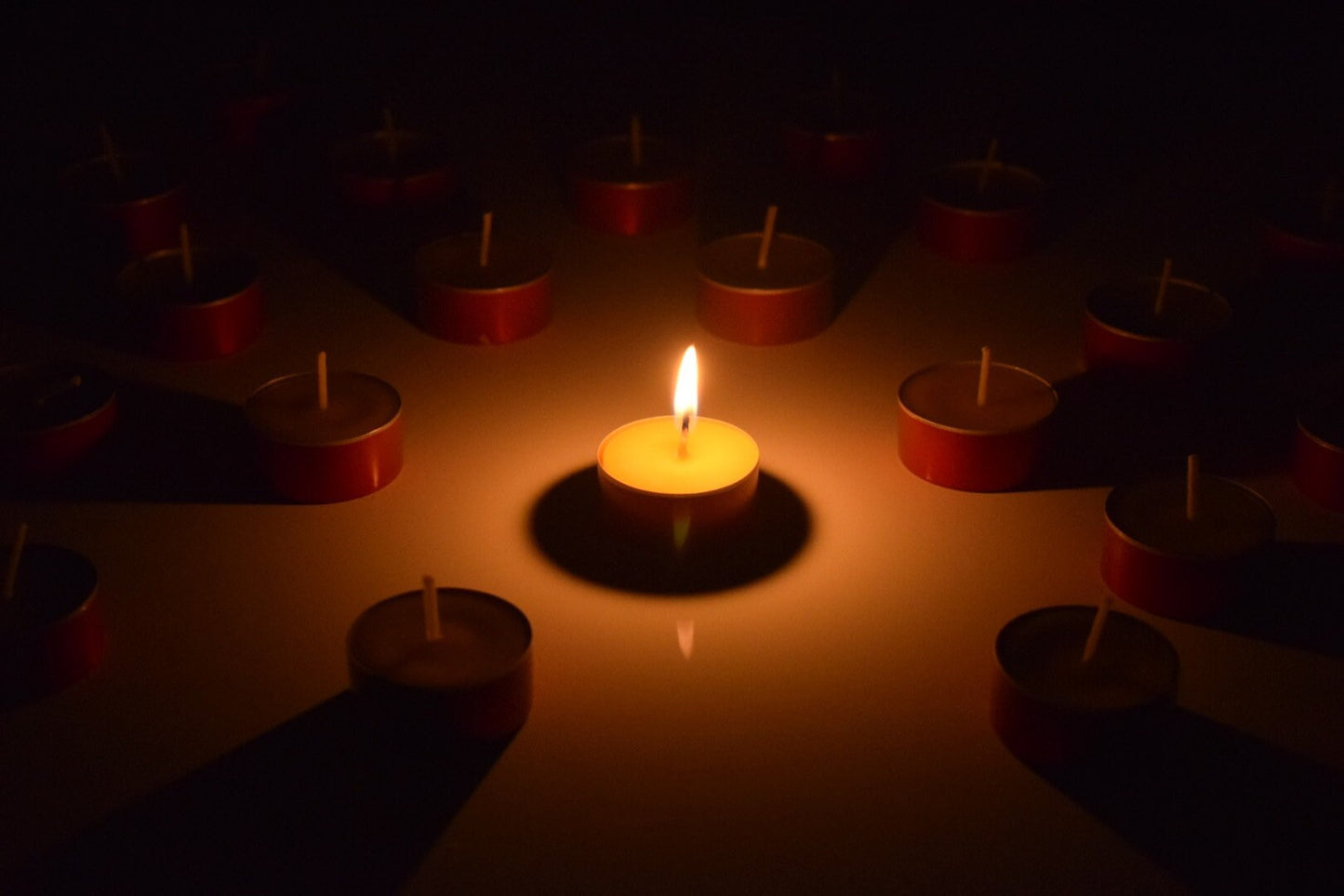 Single lit candle surrounded by unlit candles on a dark background